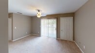 Located at 2512 Old Charlotte Hwy in Monroe, NC, this single-story unit offers a straightforward, functional layout designed for comfortable everyday living. Neutral taupe-toned walls are consistent throughout, creating a cohesive and understated aesthetic across all spaces.

The living area features wall-to-wall carpet and is anchored by a ceiling fan with an integrated light fixture. A sliding glass door with vertical blinds allows natural light to enter and provides access to an outdoor area. A secondary entry door with a hardwood-style tile landing completes the room.

The kitchen is separated from the living space by a partial wall and is accessible via a short hallway. It features warm oak cabinetry with raised-panel detailing, light speckled countertops, a white electric coil range with an overhead ventilation hood, and hardwood-style flooring. Storage is well-distributed with both upper and lower cabinet configurations.

A hallway with a louvered closet door connects the main living space to additional rooms. The bedroom includes carpet flooring and a ceiling fan, while the full bathroom is equipped with a single-sink oak vanity with a speckled countertop, a tub/shower combination, and hardwood-style flooring.