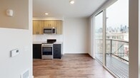 Located at 513 1st Ave N in Seattle's Lower Queen Anne neighborhood, this efficiently designed one-bedroom, one-bathroom residence makes thoughtful use of its single-floor layout. Warm wood-look flooring flows throughout, creating a cohesive feel from the entrance to the living areas.

The combined kitchen and living room serves as the heart of the unit, anchored by a well-appointed galley-style kitchen featuring two-tone cabinetry — natural wood uppers paired with dark lower cabinets — set against a crisp white subway tile backsplash. Stainless steel appliances, including a range, microwave, and refrigerator, complete the modern aesthetic. Floor-to-ceiling sliding glass doors flood the living area with natural light and open directly onto a private balcony, offering views of the Seattle skyline.

A distinctive dark accent wall near the entrance adds a bold architectural touch and leads through the unit via a clean, well-lit corridor. The bedroom is a cozy, focused retreat with recessed lighting and ample wall space. Two closets provide practical storage throughout. The bathroom features a full soaking tub and shower combo with matte black fixtures set against bright white surroundings, adding a contemporary contrast. In-unit laundry adds everyday convenience to this well-designed Seattle residence.
