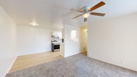 This single-floor residence offers a clean, functional layout designed for comfortable everyday living. The open living area combines light hardwood-style flooring with plush carpeting, creating a warm and inviting atmosphere. A ceiling fan overhead provides year-round comfort, while a sliding glass door floods the space with natural light and opens onto a covered balcony overlooking the surrounding area. The galley-style kitchen is efficiently designed with white cabinetry, light countertops, and stainless steel appliances including an electric range and refrigerator, complemented by a built-in dishwasher and a single-basin sink. Light hardwood flooring runs throughout the kitchen, contributing to a bright, cohesive feel. The bedrooms are carpeted and well-proportioned, each featuring neutral walls and adequate natural light. One bedroom offers direct access to a bathroom and includes a generous walk-in closet with dual hanging rods and hardwood flooring, providing excellent storage capacity. Throughout the unit, a consistent neutral color palette and clean white trim lend a timeless, move-in-ready aesthetic. The covered balcony adds an outdoor living element, offering views of the surrounding neighborhood and parking area.