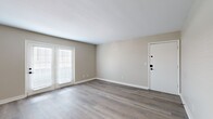 This single-floor residence offers a thoughtfully designed layout comprising two bedrooms, two bathrooms, a living room, kitchen, dedicated laundry area, hallway, and closet. The interior is finished with a consistent neutral beige palette and clean white trim, creating a cohesive, modern aesthetic throughout.

The living room is a welcoming open space featuring wood-look laminate flooring and a set of double doors fitted with white blinds, allowing natural light to filter in. The room provides comfortable space for furnishing and flows naturally through the unit.

The kitchen is efficiently laid out in a galley configuration, featuring white shaker-style cabinetry with matte black hardware, white quartz countertops, a single-basin undermount sink with a matte black faucet, and stainless steel appliances including a range, microwave, and refrigerator. Light wood-look flooring continues here, complementing the cabinetry.

The primary bedroom is a generously sized room with soft carpet, a window with blinds, and access to a walk-in closet equipped with built-in shelving and hanging rods. The second bedroom also features carpeted flooring and neutral walls.

The bathrooms are finished with white vanities, quartz countertops, matte black fixtures, and striking marble-look tile surrounding the tub and shower area, adding a refined touch to the overall design.
