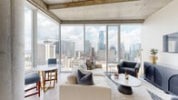 Located in the heart of Nashville at 805 Church Street, this two-bedroom, two-bathroom residence offers a compelling blend of modern design and dramatic urban views. The open-concept living, dining, and kitchen area is anchored by expansive floor-to-ceiling glass windows that frame sweeping panoramic views of the Nashville skyline, flooding the space with natural light. Exposed concrete ceilings lend an industrial-chic character to the living area, complementing the light hardwood flooring found throughout. The kitchen features contemporary cabinetry with clean lines, while the combined dining and living space provides a seamless flow ideal for both daily living and entertaining. Both bedrooms are generously proportioned, each benefiting from large windows that capture city and open-sky views. The primary bedroom includes a well-organized closet and direct access to a sleek en-suite bathroom finished with wood-look tile flooring, a floating vanity, and a backlit mirror. The second bathroom mirrors this refined aesthetic. A dedicated laundry area, multiple closets, and a connecting hallway round out the thoughtfully laid-out floor plan. The overall ambiance is contemporary and light-filled, with a distinct sense of elevated urban living in the heart of downtown Nashville.