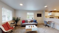 This single-floor unit offers a functional and comfortable layout across several well-defined spaces. The living room serves as the heart of the unit, featuring plush wall-to-wall carpeting, recessed lighting, and multiple windows with horizontal blinds that allow generous natural light to filter in. The space is versatile, accommodating both a seating area and a dedicated workspace. The kitchen is outfitted with ample white cabinetry accented with wood trim, continuous countertops, and a full suite of appliances including an electric range, dishwasher, and a window above the sink. Wood-look vinyl flooring runs throughout the kitchen for easy maintenance. The unit includes two well-sized bedrooms, each carpeted and equipped with windows offering outdoor views and natural light. Both rooms provide a calm, restful ambiance. The bathroom features wood-look vinyl flooring, a single-sink vanity with a mirror, and a full tub-shower combination. A separate toilet room with its own wood-look vinyl flooring provides added privacy and convenience. The overall design is clean and neutral, with warm tones and practical finishes throughout.