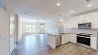 Located at 5705 Apex Dr in Fishers, Indiana, this well-appointed single-story home offers three bedrooms, two bathrooms, and a thoughtfully designed open floor plan. The kitchen is a standout feature, showcasing white shaker cabinetry, a tile backsplash, stainless steel appliances, a large peninsula with pendant lighting, and light hardwood-style flooring that flows seamlessly into the living area. The living room is filled with natural light through large windows and a glass door that opens to a balcony with tree-lined views, complemented by a ceiling fan overhead. The spacious primary bedroom features plush carpeting, abundant natural light, and access to a well-appointed en-suite bathroom complete with a dual-sink vanity, quartz-style countertops, and a walk-in tiled shower. A dedicated walk-in closet with built-in shelving and hanging rods provides excellent storage. The secondary bedrooms also feature carpet flooring and generous windows. The second bathroom includes wood-look vinyl flooring, a tiled tub-shower combo, and a white vanity. A dedicated laundry room houses a full-size washer and dryer alongside the home's mechanical systems, maximizing convenience. Neutral tones and clean finishes throughout create a cohesive, modern aesthetic.