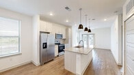 This well-appointed 1-bedroom, 1-bathroom residence offers a thoughtfully designed open-concept layout that maximizes every square foot. The kitchen serves as a central highlight, featuring a large granite-topped island with an undermount sink, sleek white cabinetry extending to the ceiling, stainless steel appliances including a French door refrigerator, electric range, and built-in microwave, all illuminated by a trio of modern pendant lights. Light wood-look flooring flows seamlessly through the kitchen and into the open living area, which is bathed in natural light from multiple windows and a set of glass French doors that open to the outdoors. A ceiling fan enhances comfort in the living space. The bedroom is carpeted for warmth and comfort, equipped with its own ceiling fan, and connects directly to the full bathroom. The bathroom offers a granite vanity with an undermount sink, light wood cabinetry, a tub-shower combination, and wood-look flooring. Two closets provide generous storage, including a walk-in closet outfitted with wire shelving systems for organized storage. The overall design is clean and contemporary, with crisp white walls and consistent finishes creating a bright, cohesive aesthetic throughout.