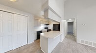Located at 140 Powers Lane in Rochester, NY, this single-floor, 2-bedroom, 1-bathroom residence offers a thoughtfully arranged layout across a compact yet functional footprint. The living room serves as a standout space, featuring soaring vaulted ceilings with exposed beam detailing and neutral gray carpet underfoot. A set of French doors floods the room with natural light and provides outdoor access, enhancing the sense of openness despite the modest scale.

The kitchen is efficiently designed with gray shaker-style cabinetry, light stone-look countertops, a peninsula with a curved breakfast bar, and black appliances including a range, dishwasher, and refrigerator. Light wood-look flooring runs through the kitchen and entry areas, while a large sliding closet nearby offers additional storage. A hallway connects the main living spaces to the bedrooms and bathroom.

The spacious primary bedroom features vaulted ceilings and natural light, while the second bedroom includes a window and plush carpet. Both rooms are finished in a soft neutral palette. The bathroom is equipped with a full soaking tub and shower combination. Throughout, the space maintains a clean, neutral aesthetic well-suited for everyday living.