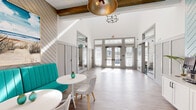 This single-floor space presents a well-designed lobby or common area with a coastal-contemporary aesthetic that blends architectural character with functional comfort. The most striking feature is the dramatically high ceiling, accentuated by exposed rustic wood beams that contrast warmly against crisp white walls and provide a sense of openness well beyond the footprint of the room.

The flooring throughout consists of light-toned wood-look planks, contributing to the airy, clean atmosphere. One wall is clad in diagonal shiplap paneling, adding textural depth and a distinct coastal flair, further reinforced by beach-themed artwork displayed above a vibrant teal upholstered bench seat.

Natural light floods the space through a wall of large French doors fitted with transom windows above, offering outdoor views and seamless connectivity to the exterior. Pendant light fixtures, including a prominent gold dome pendant and a wrought-iron chandelier, provide warm supplemental illumination.

A small seating area features a round white pedestal table paired with contemporary chairs, creating an inviting gathering spot. Additional details include a built-in counter area along one wall, glass-panel interior doors leading to adjacent spaces, and a compact vertical lift, indicating accessibility consideration. The overall ambiance is bright, welcoming, and thoughtfully appointed.