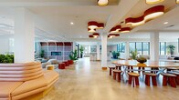 Located at 440 W State St in Columbus, Ohio, this single-floor amenity space offers a generously sized, open-plan layout designed for community gathering and flexible use. The interior is anchored by polished concrete floors that flow seamlessly throughout, lending the space a clean, contemporary character.

A striking design feature is the collection of sculptural, cloud-shaped pendant lights in deep red and warm wood tones, suspended from white ceilings across the main gathering areas. These are complemented by additional pendant clusters and recessed lighting that ensure the space is consistently well-lit.

The layout is thoughtfully zoned into distinct areas. A large lounge zone features low-profile sectional sofas arranged around a central ottaman, framed by windows that bring in views of the surrounding Columbus cityscape. Adjacent to this is a dining and collaborative zone centered on a substantial oval wood table with matching wooden stools. A long, curved banquette in blush leather runs alongside a living planter wall, paired with marble-top café tables and pendant-hung cluster lights.

The fully equipped kitchen features stainless steel appliances, white cabinetry, subway tile backsplash, a central island with bar seating, and a dedicated counter range — ideal for catering or communal use. Throughout the space, potted greenery adds warmth and vitality, reinforcing the welcoming, community-oriented ambiance.
