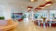 Located at 440 W State St in Columbus, Ohio, this single-floor amenity space offers a generously sized, open-plan layout designed for community gathering and flexible use. The interior is anchored by polished concrete floors that flow seamlessly throughout, lending the space a clean, contemporary character.

A striking design feature is the collection of sculptural, cloud-shaped pendant lights in deep red and warm wood tones, suspended from white ceilings across the main gathering areas. These are complemented by additional pendant clusters and recessed lighting that ensure the space is consistently well-lit.

The layout is thoughtfully zoned into distinct areas. A large lounge zone features low-profile sectional sofas arranged around a central ottaman, framed by windows that bring in views of the surrounding Columbus cityscape. Adjacent to this is a dining and collaborative zone centered on a substantial oval wood table with matching wooden stools. A long, curved banquette in blush leather runs alongside a living planter wall, paired with marble-top café tables and pendant-hung cluster lights.

The fully equipped kitchen features stainless steel appliances, white cabinetry, subway tile backsplash, a central island with bar seating, and a dedicated counter range — ideal for catering or communal use. Throughout the space, potted greenery adds warmth and vitality, reinforcing the welcoming, community-oriented ambiance.