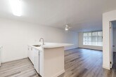 This single-story, one-bedroom, one-bathroom unit offers a well-organized layout that maximizes its compact footprint. The open-concept kitchen and living area forms the heart of the space, where a peninsula counter with an integrated sink serves as a natural divider between cooking and living zones. The kitchen is outfitted with white cabinetry extending to the ceiling, providing ample storage, along with a full suite of white appliances including a refrigerator, electric range, and microwave. Light-toned wood-look flooring runs continuously throughout the unit, lending visual cohesion and a clean, modern feel.

The living area benefits from a large picture window dressed with vertical blinds, allowing generous natural light to fill the room. A ceiling fan provides additional airflow and overhead lighting. The bedroom is a comfortable size, featuring its own large window with vertical blinds and the same wood-look flooring, creating a bright and airy atmosphere. A dedicated closet provides convenient storage.

The bathroom is clean and functional, featuring a combined tub-shower unit, toilet, and a vanity with a white countertop. Throughout the unit, crisp white walls and consistent finishes contribute to a bright, cohesive, and move-in-ready environment.