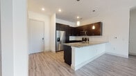 Located at 6001 S Congress Ave in Austin, TX, this single-floor unit offers a thoughtfully designed layout with contemporary finishes throughout. The open-concept kitchen serves as a central highlight, featuring dark espresso cabinetry extending to the ceiling, granite countertops, a large peninsula with an undermount sink, stainless steel appliances including a French door refrigerator and built-in microwave, and elegant pendant lighting that adds a warm, modern touch. Light wood-look flooring flows seamlessly through the main living and kitchen areas, enhancing the bright, airy atmosphere created by recessed lighting and neutral wall tones. The spacious living area benefits from a ceiling fan, sliding glass doors that invite natural light and outdoor access, and generous floor space well-suited for a variety of layouts. Bedrooms feature plush carpeting and large windows fitted with blinds for privacy and light control. The bathrooms are finished with matching dark cabinetry, granite countertops, undermount sinks, large mirrors, and tiled walk-in showers. A dedicated in-unit laundry area with full-size washer and dryer hookups and built-in shelving adds everyday convenience. The overall design strikes a clean, modern aesthetic throughout.