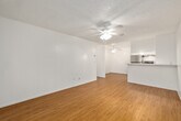 This single-story, one-bedroom, one-bathroom unit offers a well-organized layout across a compact but efficiently utilized floor plan. Hardwood-style flooring runs consistently throughout all rooms, providing a cohesive aesthetic and easy maintenance.

The living room is a comfortable, open space featuring a ceiling fan with light fixture, neutral white walls, and a large window dressed with vertical blinds that frame views of surrounding greenery. A wall-unit air conditioner provides climate control. The room offers a clean, versatile space for various furniture arrangements.

The kitchen is functionally equipped with stainless steel appliances, including a full-size refrigerator and electric range. White cabinetry extends to the ceiling, maximizing storage capacity, while a granite-style countertop adds a polished touch. A ceiling fan is positioned in the adjacent dining area.

The bedroom is a well-proportioned room featuring hardwood-style flooring, a ceiling fan, a window with vertical blinds offering outdoor views, and a mirrored sliding closet that enhances the sense of space while providing practical storage.

The bathroom includes a white vanity with a granite-style countertop, a medicine cabinet with mirror, and a separate water closet with a combination tub and shower. Chrome fixtures and white cabinetry maintain a clean, uniform finish throughout.