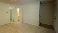 This two-floor residential space offers a straightforward and functional layout with a clean, neutral aesthetic throughout. The interior is finished in soft cream and beige tones, creating a calm and cohesive atmosphere from room to room.

The upper level features a spacious carpeted room with light beige wall-to-wall carpeting that adds warmth underfoot. A paneled white door opens to an attached bathroom, which is illuminated by interior lighting and includes visible cabinetry, suggesting practical storage. The bathroom's bright finish contrasts neatly with the softer tones of the main room. A staircase is accessible directly from this level, connecting seamlessly to the lower floor and featuring carpet-covered treads that maintain the consistent flooring aesthetic.

The walls throughout are painted in a light cream tone, kept clean and unadorned to maximize the sense of openness. White baseboard trim lines the perimeter of the rooms, providing a crisp finish to the flooring transitions. The overall layout appears efficient, with doorways and hallways that allow for easy movement between spaces.

The space's two-floor configuration provides natural separation between living areas, offering versatility in how each level can be used. The understated design and neutral palette make the space adaptable to a variety of furnishing styles and functional needs.