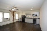 This single-floor unit offers an open-concept layout defined by rich, dark hardwood floors that extend throughout the main living area. The space is bright and airy, benefiting from multiple windows that allow natural light to fill the room. A ceiling fan with an integrated light fixture is centrally positioned overhead, providing both ventilation and ambient lighting.

A standout architectural detail is the exposed brick column accent wall, which adds a historic, industrial character to the otherwise clean and neutral interior. The walls are finished in crisp white, complementing the dark flooring and creating a balanced contrast throughout.

The kitchen is seamlessly integrated into the main living space and features gray cabinetry, dark countertops, and black appliances including a refrigerator, gas range, and microwave. A double basin sink and a dedicated in-unit washer are also included, adding functional convenience.

The bathroom is compact and efficiently designed, featuring a stand-up shower stall with built-in shelving, chrome fixtures, a wall-mounted sink, and a large mirror. The unit also includes a dedicated electrical panel and a wall-mounted air conditioning unit, ensuring year-round comfort.