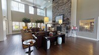 Located at 9419 Cumberland Dr in Fredericksburg, Virginia, this single-story community clubhouse serves as a welcoming social hub for residents. The grand entrance lobby immediately impresses with soaring double-height ceilings, abundant natural light from expansive windows, and rich dark hardwood flooring that flows throughout the entire space. Large decorative indoor trees flank the entryway, adding a natural, organic warmth to the airy surroundings.

The centerpiece of the main lounge is a dramatic floor-to-ceiling stacked stone fireplace, complemented by a rustic wood mantel and framed artwork. Plush leather sofas, accent chairs, and carefully chosen furnishings create an inviting seating arrangement ideal for relaxation and socializing. French doors connect the lounge to the adjacent dining and café area, which features a mix of standard round tables and elevated bar-height seating, all set against warm, neutral-toned walls.

A fully equipped kitchen with dark cabinetry, granite countertops, a mosaic tile backsplash, and stainless steel appliances supports community gatherings and events. A cozy library nook offers built-in bookshelves, a wall-mounted television, and intimate seating. A dedicated coffee and refreshment bar rounds out the amenities, making this clubhouse a comprehensive and well-appointed community gathering space.
