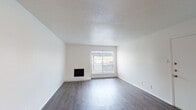 This single-floor residence offers a well-organized layout with clearly defined living spaces throughout. The main living area is a standout feature, boasting dark hardwood-style flooring, crisp white walls, and a textured ceiling that adds subtle character. A built-in fireplace set against a painted brick accent wall serves as the room's focal point, complemented by a window fitted with horizontal blinds that allows natural light to fill the space. An open passageway leads to a dining area with warm-toned hardwood-style flooring, a ceiling light fixture, and vertical blinds offering additional light control. The kitchen is functional and well-appointed, featuring white cabinetry with brushed nickel hardware, white countertops, a stainless steel double-basin sink, a subway tile backsplash, and a stainless steel dishwasher — providing ample storage and prep space. The bedroom is generously sized with plush neutral carpeting and a clean, minimalist design. Accessible from the bedroom, the bathroom includes a vanity with white cabinetry, a large framed mirror, and Hollywood-style lighting, with a walk-in closet conveniently positioned nearby. Throughout, the space maintains a neutral, move-in-ready aesthetic with a consistent clean and bright ambiance.