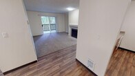 This single-floor residence at 9901–10099 S 249th Pl in Kent, WA offers a practical and comfortable layout across several well-defined living spaces. The main living area is a standout feature, combining wood-style hard flooring near the entryway with plush carpeting throughout the primary gathering space. A fireplace serves as a central focal point, while a sliding glass door opens to a private balcony, allowing natural light to filter in and providing views of surrounding greenery.

The kitchen is efficiently designed, featuring warm wood-toned cabinetry, ample upper and lower storage, a coil-burner electric range, a full-size refrigerator, and light-toned countertops. Wood-style flooring carries through this space, complementing the cabinetry tones.

The bedrooms vary in character. One features dual windows that frame outdoor views and flood the room with natural light, while another offers a cozier feel with a single window and carpeted floors. An additional room with wood-style flooring provides flexible use as a bedroom or office.

The bathroom includes a well-lit vanity with a large mirror, light-toned countertop, and a grab bar. Textured ceilings are consistent throughout, and baseboard heating is present in select rooms, contributing to a straightforward and functional overall ambiance.
