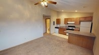 This single-floor space is designed with an open-concept layout that seamlessly connects the living area and kitchen, creating a functional and cohesive environment. The living area is finished with wall-to-wall carpet, providing a comfortable and warm underfoot feel, while vaulted ceilings add a sense of height and openness to the space. A ceiling fan with a light fixture is centrally positioned, offering both air circulation and ambient lighting, complemented by recessed lighting throughout.

The kitchen is efficiently arranged with warm-toned oak cabinetry offering ample storage, laminate countertops, and a full suite of appliances including an electric range, built-in microwave, and dishwasher. A peninsula counter extends into the open area, providing additional workspace and a casual dining or seating option. The kitchen transitions smoothly into the living space without visual barriers, enhancing the overall sense of roominess.

A bathroom is conveniently accessible directly from the main living area and is finished with tile flooring and standard fixtures. An electrical panel is also visible within the main living space. Neutral wall tones throughout the unit create a clean, versatile backdrop well-suited for a variety of interior styles.
