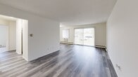 This single-floor residence offers a bright and functional layout designed for comfortable everyday living. The open living and dining area is finished with grey hardwood-style flooring that extends throughout the main living spaces, lending a modern, cohesive feel. A large sliding glass door floods the room with natural light and provides views of the outdoors, while vertical blinds offer adjustable privacy. A wall-unit air conditioner and baseboard heating ensure year-round comfort.

The galley-style kitchen is efficiently arranged with white cabinetry lining both walls, light countertops, a single-basin sink, and white appliances including a range and refrigerator. The layout maximizes storage and workspace within a compact footprint.

The bedrooms are carpeted for warmth and comfort, each featuring bifold closet doors that open to well-organized closet spaces with shelving and hanging rods. The rooms are bright, neutral, and generously sized.

The bathroom is neatly appointed with mosaic tile flooring, white tiled walls in the shower/tub area, a wood-toned vanity with a wide countertop, a large framed mirror, and updated fixtures. Grab bars in the shower area add an accessibility-conscious touch. Overall, the unit presents a clean, move-in ready environment with practical finishes throughout.