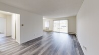 This single-floor residence offers a bright and functional layout designed for comfortable everyday living. The open living and dining area is finished with grey hardwood-style flooring that extends throughout the main living spaces, lending a modern, cohesive feel. A large sliding glass door floods the room with natural light and provides views of the outdoors, while vertical blinds offer adjustable privacy. A wall-unit air conditioner and baseboard heating ensure year-round comfort.

The galley-style kitchen is efficiently arranged with white cabinetry lining both walls, light countertops, a single-basin sink, and white appliances including a range and refrigerator. The layout maximizes storage and workspace within a compact footprint.

The bedrooms are carpeted for warmth and comfort, each featuring bifold closet doors that open to well-organized closet spaces with shelving and hanging rods. The rooms are bright, neutral, and generously sized.

The bathroom is neatly appointed with mosaic tile flooring, white tiled walls in the shower/tub area, a wood-toned vanity with a wide countertop, a large framed mirror, and updated fixtures. Grab bars in the shower area add an accessibility-conscious touch. Overall, the unit presents a clean, move-in ready environment with practical finishes throughout.