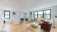 This thoughtfully designed single-floor residence combines contemporary finishes with a bright, open layout. Herringbone-patterned hardwood flooring flows seamlessly throughout the space, lending warmth and visual continuity to every room.

The open-plan living and dining area is anchored by large black-framed windows that invite generous natural light and offer pleasant views of the surrounding neighborhood. The living space provides ample room for comfortable seating arrangements, while the adjacent dining area features its own window nook, creating a welcoming setting for meals.

The sleek, all-white kitchen is a standout feature, outfitted with flat-front cabinetry that extends to the ceiling, stainless steel appliances, and a clean white countertop island with bar seating — ideal for casual dining or entertaining. A second window frames views of the rooftops beyond, adding architectural character.

Two well-proportioned bedrooms offer a calm retreat, each with black-framed windows, recessed lighting, and built-in closet storage. The primary bedroom features herringbone flooring and a serene, neutral palette.

The bathroom is finished with hexagonal mosaic tile flooring, a floating white vanity with illuminated mirrors, and a tiled shower, delivering a clean, modern aesthetic. Throughout the residence, recessed lighting and a crisp white color palette reinforce a refined, contemporary ambiance.