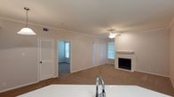 This single-floor residence in Lewisville offers a well-designed layout with a comfortable, cohesive flow between spaces. The living area serves as the heart of the home, showcasing plush carpeted flooring, crown molding, and a classic tiled fireplace with a raised hearth — a standout feature that adds warmth and character to the room. A ceiling fan overhead provides both functionality and a finished look to the space. Natural light filters in through multiple windows dressed with horizontal blinds, brightening the interior throughout the day. Vertical blinds adorn the sliding door or large window panel, offering flexible light control and a connection to the outdoors. The kitchen opens directly to the living area, featuring light countertops and a modern faucet, making it ideal for everyday convenience and easy entertaining. A louvered closet door near the entryway provides practical storage, while a doorway leads into an additional carpeted room — likely a bedroom — that also benefits from natural window light. Crown molding carries consistently through the space, lending a polished, cohesive aesthetic. Overall, the residence presents a clean, neutral palette ready for personalization.