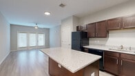 This single-story residence offers a well-designed open layout with light wood-style flooring throughout, creating a cohesive and airy atmosphere across the living spaces. The kitchen serves as a central highlight, outfitted with rich dark espresso cabinetry, light granite countertops, and a full suite of black appliances including a refrigerator, range, microwave, and dishwasher. A generously sized center island with matching granite provides additional prep space and casual seating potential. Recessed lighting illuminates the kitchen, which flows seamlessly into the living area.

The living room is bright and open, benefiting from a ceiling fan and French doors fitted with blinds that invite natural light while offering privacy and outdoor access. Neutral-toned walls complement the light flooring throughout.

The bedroom is spacious and well-lit by a large window, accompanied by a substantial walk-in closet featuring wire shelving for organized storage. The bathroom is elegantly appointed with a dark vanity topped with granite, a glass-enclosed tiled walk-in shower, and large-format tile flooring, combining practicality with a clean, modern aesthetic.