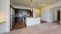 This single-floor residence offers a thoughtfully designed layout that balances open communal spaces with comfortable private areas. The kitchen serves as a standout feature, showcasing rich dark-espresso cabinetry extending to the ceiling, stainless steel appliances including a gas range and built-in microwave, a tile backsplash, and granite-style countertops. A central island with pendant lighting provides additional workspace and an informal dining option, while track lighting illuminates the area effectively. Durable hardwood-style flooring runs throughout the kitchen, transitioning to plush neutral carpeting in the living and bedroom areas.

The bedrooms are generously proportioned, each offering large windows that invite natural light and views of the surrounding neighborhood. Ceiling fans are present in select rooms for added comfort. At least one bedroom features a spacious walk-in closet outfitted with adjustable wire shelving on multiple levels, providing ample organizational flexibility.

The bathrooms are finished consistently, featuring large-format dark tile flooring, white subway-tiled tub-and-shower combinations accented with mosaic tile borders, white cabinetry, and marble-style countertops, creating a clean and polished aesthetic throughout.