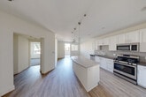 Located at 111 W Harrison St in Corona, CA, this thoughtfully designed one-bedroom, one-bathroom unit offers a well-utilized floor plan across a single level. The open-concept living and kitchen area serves as the heart of the home, anchored by a curved granite-topped center island illuminated by stylish pendant lighting. The kitchen is outfitted with white shaker cabinetry, a gray subway tile backsplash, dark countertops, and a full suite of stainless steel appliances including a gas range, microwave, dishwasher, and refrigerator. Wood-look flooring flows throughout the main living areas, adding warmth and continuity to the space. Natural light pours in through large windows, offering views of the palm tree-lined neighborhood and the surrounding modern architectural landscape. The bedroom features plush carpeting, a generously sized window framing outdoor greenery, and access to a dedicated closet. The bathroom is clean and functional, complete with a tiled tub-shower combo, a white vanity with under-sink storage, and a large mirror. A hallway connects the private spaces, maintaining an efficient and comfortable flow throughout the unit.