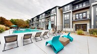 Located at 950 Marietta St NW in Atlanta's dynamic Westside neighborhood, this outdoor amenity space offers a well-appointed retreat designed for relaxation and social gatherings. At the heart of the area is a generously sized resort-style swimming pool with vivid turquoise water, surrounded by a spacious concrete sundeck furnished with a mix of classic lounge chairs and striking teal modern seating, providing ample space for sunbathing and leisure. The pool area is framed by lush landscaping and mature trees that offer seasonal color and a sense of privacy. Adjacent to the pool, a dedicated outdoor living area serves as an entertainment hub, featuring a built-in gas grill station, a substantial stone fireplace with a mounted flat-screen television above, and additional lounge seating arranged for comfort and conversation. The surrounding multi-story building showcases a contemporary architectural design with dark gray and white exterior tones, large windows, and private balconies that overlook the amenity courtyard. Iron fencing encloses the space, creating a secure and cohesive environment. Together, these features combine to create a functional and visually appealing outdoor destination suited for both everyday use and social events.