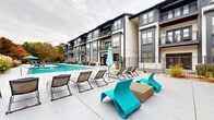Located at 950 Marietta St NW in Atlanta's dynamic Westside neighborhood, this outdoor amenity space offers a well-appointed retreat designed for relaxation and social gatherings. At the heart of the area is a generously sized resort-style swimming pool with vivid turquoise water, surrounded by a spacious concrete sundeck furnished with a mix of classic lounge chairs and striking teal modern seating, providing ample space for sunbathing and leisure. The pool area is framed by lush landscaping and mature trees that offer seasonal color and a sense of privacy. Adjacent to the pool, a dedicated outdoor living area serves as an entertainment hub, featuring a built-in gas grill station, a substantial stone fireplace with a mounted flat-screen television above, and additional lounge seating arranged for comfort and conversation. The surrounding multi-story building showcases a contemporary architectural design with dark gray and white exterior tones, large windows, and private balconies that overlook the amenity courtyard. Iron fencing encloses the space, creating a secure and cohesive environment. Together, these features combine to create a functional and visually appealing outdoor destination suited for both everyday use and social events.