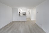 This well-appointed unit on Battlefield Road in Mississauga presents a clean, modern aesthetic defined by a consistent light wood laminate flooring and crisp white walls throughout. The open living area is a standout feature, bathed in natural light from a large floor-to-ceiling sliding glass door that opens directly onto a private balcony. Vertical blinds provide adjustable light control, while views of mature trees and green communal grounds enhance the sense of openness. A wall-mounted climate control unit ensures year-round comfort in this space.

The kitchen is thoughtfully designed in a galley layout, outfitted with sleek white cabinetry, light stone countertops, and a full suite of stainless steel appliances, including a refrigerator, electric range, built-in microwave, and dishwasher. Pendant and flush-mount lighting add a polished finish to the workspace.

The bedroom is a generously sized, quiet retreat featuring a large sliding-door closet with built-in shelving and a dedicated window with an outdoor view and roller shade. Additional spaces visible in the floor plan include a full bathroom and in-unit laundry. The overall ambiance is bright, clean, and functional, making efficient use of a well-organized single-floor layout.