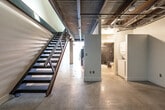 This single-floor loft showcases a striking industrial aesthetic throughout its well-planned layout. Polished concrete floors run seamlessly across the entire space, complementing the exposed concrete ceiling complete with visible ductwork, conduit, and track lighting — hallmarks of urban loft design. The open-plan living area is generously proportioned, bathed in natural light from large windows that frame views of surrounding greenery, and features a clean expanse of white walls that offer a versatile canvas.

The kitchen is thoughtfully designed with light maple cabinetry extending to the ceiling for ample storage, dark granite countertops, and a full suite of stainless steel appliances including a gas range, over-the-range microwave, and a full-size refrigerator. A stacked washer and dryer unit is conveniently located adjacent to the kitchen area, adding practical in-unit laundry access.

The bathroom features a full tub-shower combination accented by bold dark slate tile surround, a light wood vanity with a dark countertop, and concrete flooring that maintains the cohesive industrial feel. The overall ambiance of this loft is modern and urban, blending raw architectural elements with functional, contemporary finishes.
