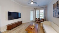 Located at 2200 Pooler Parkway in Pooler, Georgia, this 1-bedroom, 1-bathroom residence offers a cohesive and modern living experience across a single, efficiently designed floor. The welcoming entrance opens into a bright living room finished with light hardwood-style flooring, crown molding, and a ceiling fan. Large windows with stylish grid-patterned curtains invite natural light while offering outdoor views, and a glass door provides direct exterior access. The kitchen is a standout feature, showcasing dark granite countertops, a large undermount sink, stainless steel appliances, and a two-tone cabinet design combining white upper cabinetry with warm wood lower cabinets, complemented by a classic tile backsplash and pendant lighting. The spacious bedroom features crown molding, a ceiling fan, and generous natural light, and connects directly to a well-sized walk-in closet outfitted with wire shelving systems and hardwood-style flooring for practical storage. The bathroom is clean and functional, offering a wood-toned vanity with white countertops, a glass-enclosed shower, and light tile flooring. Neutral tones and consistent finishes throughout the space create a calm, cohesive ambiance suited for comfortable everyday living.