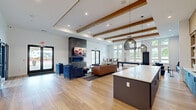 This single-floor community space offers a generously sized, thoughtfully designed interior that seamlessly blends lounge, dining, and meeting functions. The main living area features exposed wood ceiling beams, recessed lighting, and light hardwood flooring that runs throughout. A dramatic floor-to-ceiling concrete fireplace serves as the room's focal point, flanked by plush blue armchairs and a leather sofa. Adjacent to the lounge is a game area with a billiards table, surrounded by large windows that flood the space with natural light and provide views of the surrounding landscape.

The kitchen island, topped with a crisp white quartz surface and accented by navy cabinetry and woven pendant lights, anchors the entertaining zone. Built-in wood shelving and an integrated television complete the setup. A bold blue banquette with channel-tufted detailing runs along one wall, offering casual seating near the kitchen.

The two dining areas offer distinct experiences—one features a large communal table with circular ring pendant lighting and floor-to-ceiling windows, while semi-private live-edge booths with geometric blue wallcovering provide intimate seating. A separate conference room, also adorned with the distinctive patterned wallcovering, accommodates a full meeting table with ample seating and outdoor views.