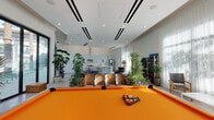 Located on Winnetka Ave in Chatsworth, Los Angeles, this single-floor space offers a thoughtfully designed open-plan interior with a clean, modern aesthetic. Polished terrazzo flooring flows throughout, reflecting natural light and adding a distinctive architectural character to every area.

The kitchen is a standout feature, equipped with soft blue-grey shaker cabinetry, a white subway tile backsplash, stainless steel appliances including a full-size refrigerator with ice and water dispenser, a gas range with overhead hood, and a spacious white-topped island with bar seating — ideal for both casual dining and entertaining.

The main living area is generously proportioned with soaring ceilings and large windows draped in sheer curtains that bathe the space in diffused natural light. A large sectional sofa anchors the lounge, complemented by a glass coffee table and an array of lush indoor plants that bring warmth and texture to the contemporary setting.

A dedicated entertainment and recreation zone includes a bold orange-felted pool table, an arcade machine, and multiple large-screen televisions. A classic Eames lounge chair and ottoman alongside well-stocked bookshelves complete the media and reading nook. The overall ambiance is bright, open, and versatile — suited for both relaxed gatherings and active entertainment.
