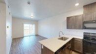 Located in Pasco, WA, this well-appointed 3-bedroom, 2-bathroom residence offers a thoughtfully designed single-level layout with modern finishes throughout. The open-concept kitchen and living area serves as the heart of the home, where rich dark-toned cabinetry, white quartz countertops, a subway tile backsplash, and black stainless steel appliances create a contemporary and functional cooking space. A large kitchen island with an integrated sink adds both workspace and visual appeal. The living area extends from the kitchen and features light wood-look flooring, neutral walls, and a sliding glass door that opens to a private balcony, filling the space with natural light and outdoor views. The three bedrooms are carpeted for comfort, each featuring windows with blinds that allow in natural light while maintaining privacy. The spacious primary bedroom includes a closet with sliding panel doors. Two clean, well-finished bathrooms feature wood-look flooring, walk-in showers, and brushed nickel fixtures. Crisp white walls and panel-style interior doors maintain a consistent, clean aesthetic throughout the home, making it a bright and inviting living space.