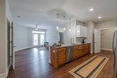 This single-floor residence offers a thoughtfully designed open-concept layout that seamlessly connects the kitchen and living area. The kitchen serves as a central focal point, featuring a large granite-topped island with an undermount sink, pendant lighting, white upper cabinetry, warm wood-toned lower cabinetry, subway tile backsplash, and a full suite of stainless steel appliances including a French door refrigerator, range, and built-in microwave. The open living area extends naturally from the kitchen and is filled with natural light from glass French doors, complemented by a ceiling fan overhead. Rich hardwood flooring flows consistently throughout the entire space, adding warmth and cohesion. The two bedrooms are generously sized, each equipped with ceiling fans and windows that bring in natural light. The primary bathroom features a granite vanity, a walk-in shower with grab bars, white cabinetry, and a large mirror. The second bathroom offers a full tub-shower combination with stylish curtain accents and matching granite countertops. A dedicated laundry room with a full-size washer and dryer and wire shelving adds everyday convenience. The space is finished with clean white trim, neutral walls, and a bright, modern aesthetic throughout.