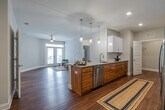 This single-floor residence offers a thoughtfully designed open-concept layout that seamlessly connects the kitchen and living area. The kitchen serves as a central focal point, featuring a large granite-topped island with an undermount sink, pendant lighting, white upper cabinetry, warm wood-toned lower cabinetry, subway tile backsplash, and a full suite of stainless steel appliances including a French door refrigerator, range, and built-in microwave. The open living area extends naturally from the kitchen and is filled with natural light from glass French doors, complemented by a ceiling fan overhead. Rich hardwood flooring flows consistently throughout the entire space, adding warmth and cohesion. The two bedrooms are generously sized, each equipped with ceiling fans and windows that bring in natural light. The primary bathroom features a granite vanity, a walk-in shower with grab bars, white cabinetry, and a large mirror. The second bathroom offers a full tub-shower combination with stylish curtain accents and matching granite countertops. A dedicated laundry room with a full-size washer and dryer and wire shelving adds everyday convenience. The space is finished with clean white trim, neutral walls, and a bright, modern aesthetic throughout.