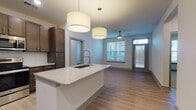 Located at 8320 University Executive Park Dr in Charlotte, NC, this single-floor unit offers a well-designed, open-concept layout suited for comfortable everyday living. The kitchen serves as a central highlight, featuring rich dark-brown cabinetry extending to the ceiling, stainless steel appliances including a refrigerator, range, and built-in microwave, and a large island with granite countertops and an integrated sink with a professional-style faucet. Pendant drum lighting illuminates the island and flows naturally into the adjoining living area, which benefits from natural light provided by windows fitted with horizontal blinds and a ceiling fan overhead. Light wood-style flooring runs throughout the main living and kitchen areas, creating a cohesive, contemporary aesthetic. The bedrooms are carpeted, offering a softer feel, and each is equipped with windows that bring in natural light and views of the surrounding area, with ceiling fans for added comfort. The bathrooms are finished with large-format light tile flooring, dark wood vanities with granite countertops, and chrome fixtures. One bathroom features a glass-enclosed walk-in shower, while the other offers a tiled tub-shower combination. The overall ambiance is clean, modern, and functional.