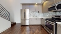 This three-story space showcases a clean, contemporary design with dark hardwood-style flooring and crisp white walls carried consistently throughout all levels. A modern staircase with dark wood treads and sleek metal railings serves as a connecting architectural element, complemented by louvered storage closets along the hallway for practical organization.

The kitchen is well-appointed with stainless steel appliances, including a gas range, over-the-range microwave, and a French door refrigerator. Taupe flat-front cabinetry pairs with a mosaic tile backsplash and light quartz countertops, creating a polished, functional cooking space.

Bedrooms feature recessed lighting, natural light from well-placed windows, and direct access to bathrooms. One full bathroom includes large-format subway tile surrounding a soaking tub and shower combination, a single-sink vanity with quartz countertop, and warm wood cabinetry with brushed nickel hardware. A separate powder room on another level provides additional convenience with a matching vanity and mirror. The overall ambiance across all three floors is modern, light-filled, and cohesive.