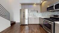 This three-story space showcases a clean, contemporary design with dark hardwood-style flooring and crisp white walls carried consistently throughout all levels. A modern staircase with dark wood treads and sleek metal railings serves as a connecting architectural element, complemented by louvered storage closets along the hallway for practical organization.

The kitchen is well-appointed with stainless steel appliances, including a gas range, over-the-range microwave, and a French door refrigerator. Taupe flat-front cabinetry pairs with a mosaic tile backsplash and light quartz countertops, creating a polished, functional cooking space.

Bedrooms feature recessed lighting, natural light from well-placed windows, and direct access to bathrooms. One full bathroom includes large-format subway tile surrounding a soaking tub and shower combination, a single-sink vanity with quartz countertop, and warm wood cabinetry with brushed nickel hardware. A separate powder room on another level provides additional convenience with a matching vanity and mirror. The overall ambiance across all three floors is modern, light-filled, and cohesive.