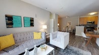 Located at 1980 Marlton Pike East in Cherry Hill, NJ, this single-floor unit offers a thoughtfully designed open-concept layout that seamlessly connects the living, dining, and kitchen areas. The living room is a welcoming space, featuring neutral-toned walls, recessed lighting, and rich hardwood-style flooring that runs throughout the unit. The room comfortably accommodates generous seating arrangements, and its open sightlines create a bright and airy atmosphere. Colorful wall art adds a vibrant accent to the understated, contemporary décor. The kitchen is efficiently designed with warm wood-toned cabinetry, a tile backsplash, and stainless steel appliances, including a refrigerator and microwave. A peninsula with bar seating provides a casual dining option, while a dedicated dining area with a glass-top table and seating sits adjacent, making the space ideal for both everyday meals and entertaining. The consistent hardwood-style flooring and clean white trim tie the spaces together cohesively. The unit's single-floor layout ensures easy accessibility and a practical flow between all areas. Overall, the space strikes a balance between modern functionality and comfortable, stylish living in a well-located Cherry Hill address.