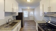 Located at 435 Lambeth Dr in Charlotte, NC, this single-floor home offers a clean, updated interior with a cohesive neutral color palette and modern finishes throughout. The living areas feature rich, dark hardwood-style flooring that contrasts beautifully with light gray walls and crisp white trim, creating a welcoming and contemporary atmosphere. Natural light filters in through white-blinded windows, enhancing the open and airy feel of each room. The kitchen is a functional highlight, equipped with white cabinetry fitted with sleek bar-pull hardware, granite-look countertops, and stainless steel appliances including a refrigerator and range. A windowed back door provides additional natural light and easy access to the exterior. The bathroom is neatly appointed with a tiled tub-shower surround, granite-topped vanity, a large mirror, and a bright window that keeps the space feeling fresh. Carpeted bedroom areas offer a softer, comfortable retreat, with windows providing natural light and a quiet ambiance. Textured ceilings are consistent throughout the home, adding a classic residential character. Overall, this home presents a well-maintained, move-in ready space with practical updates and a straightforward, comfortable layout.