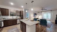 This thoughtfully designed single-story residence offers a modern, open-concept layout that seamlessly connects the kitchen, dining, and living areas. The kitchen is a standout feature, outfitted with rich dark-toned cabinetry, granite countertops, stainless steel appliances, and a generous island with bar seating — all illuminated by pendant lighting overhead. The living area flows naturally from the kitchen and is highlighted by a stylish barn door, a ceiling fan, and warm wood-look flooring throughout.

The bedrooms are comfortable and well-lit, each featuring plush carpeting and windows that invite natural light. One bedroom serves as a versatile office or flex space with wood-look flooring and sheer window treatments. The primary bathroom includes a walk-in glass shower, granite vanity countertop, dark cabinetry, and wood-look flooring. A secondary bathroom mirrors the same refined finishes, featuring a soaking tub with shower combination and matching granite countertop vanity.

A dedicated laundry room provides added convenience with a full-size washer and dryer. Throughout the residence, a consistent palette of white walls, dark cabinetry, and light wood-look flooring creates a cohesive, contemporary aesthetic.