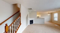 This two-floor home offers a well-organized layout with functional design throughout. The main level centers around an open living area with plush carpeting and a corner fireplace, creating a welcoming focal point. The adjacent kitchen features white cabinetry, a coil-burner range, built-in microwave, refrigerator, and a peninsula with a countertop overhang ideal for casual dining. Light tile flooring runs through the kitchen, which also provides direct access to a laundry or utility area. A half bathroom on the main level is finished with tile flooring, a pedestal sink, and a well-lit vanity mirror. A classic wood-railed staircase leads to the upper floor, where multiple carpeted bedrooms offer natural light through blinds-fitted windows. The primary bedroom includes dual closets and a ceiling fan, while additional bedrooms also feature carpet and generous window placement. The upper-level full bathroom is equipped with a double-sink vanity with ample counter space, white cabinetry, tile flooring, and a tub-shower combination. Neutral tones and textured ceilings carry throughout both floors, contributing to a clean, consistent aesthetic suited to a variety of interior styles.