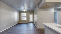 This thoughtfully designed one-bedroom, one-bathroom unit offers a functional and comfortable single-floor layout. The open-concept living and kitchen area serves as the heart of the home, featuring dark hardwood-style flooring, neutral gray walls, a textured ceiling, and a ceiling fan with light fixture. Natural light flows in through multiple windows fitted with blinds, and a glass-panel entry door connects the living area to the outdoors.

The kitchen is equipped with white cabinetry, speckled countertops, a peninsula with a double-basin sink, and black appliances including a refrigerator, range, microwave, and dishwasher. A range hood is positioned above the cooking area, and the open layout allows for easy interaction with the living space.

A hallway leads to the bedroom, bathroom, and utility room. The carpeted bedroom is generously sized with a ceiling fan, a large window offering outdoor views, and direct access to both a walk-in closet with wire shelving and the full bathroom. The bathroom includes a single-sink vanity with speckled countertop, a mirror, and a tub-shower combination with grab bars. The utility room provides washer and dryer hookups. Two closets offer ample storage throughout the unit.