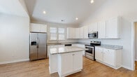 Located at 2314 Doveshell Dr in North Myrtle Beach, SC, this single-story home offers a bright and well-designed layout with consistent warm hardwood-style flooring running throughout. The open-concept kitchen is a standout feature, showcasing white shaker cabinetry, granite countertops, a central island with additional storage, and a full suite of stainless steel appliances including a refrigerator with ice maker, electric range, microwave, and dishwasher. Vaulted ceilings in the kitchen amplify the sense of space, while recessed lighting and natural light from multiple windows create a clean, airy atmosphere. The living area greets you at the entry with soaring vaulted ceilings, a ceiling fan, a paneled front door with transom window, and generous natural light from multiple windows with blinds. The bedrooms are well-proportioned, each featuring vaulted or elevated ceilings, ceiling fans, and bright windows. The bathrooms are finished with granite-topped vanities and white cabinetry, with one bathroom offering a glass-enclosed shower and another featuring a full soaking tub-shower combination. The home's neutral color palette and cohesive finishes throughout lend a clean, move-in-ready appeal.