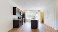 Located at Riverside Foundry on West Market Street in Marietta, Pennsylvania, this two-floor residence offers a well-appointed layout with contemporary finishes throughout. The heart of the home is an open-concept kitchen, showcasing rich dark espresso cabinetry, striking granite countertops, and stainless steel appliances including a range, microwave, and refrigerator. A central island with a undermount sink and pendant lighting above serves as both a functional workspace and a natural gathering point. Large windows at the rear of the kitchen flood the space with natural light and provide views of an outdoor deck. Hardwood-style flooring runs throughout the main living areas, lending a clean, cohesive aesthetic. A conveniently located bathroom on the main level features a dark vanity with granite countertop and hardwood-style flooring. Upstairs, the bedrooms are finished with plush carpeting and include closet storage, while a ceiling fan with light fixture adds comfort to the main bedroom. A dedicated bathroom on the upper level is equipped with a walk-in shower stall. The overall design balances modern elegance with practical functionality in a residential community setting.