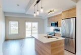 Located on University Avenue NW in Edmonton, Alberta, this well-appointed 3-bedroom, 2-bathroom unit offers a clean, contemporary design throughout its single-floor layout. Light wood laminate flooring runs seamlessly across all rooms, complementing the crisp white walls and creating a bright, cohesive aesthetic.

The open-concept kitchen features a light wood island with an integrated sink, pendant lighting overhead, and stainless steel appliances, flowing naturally into the main living area. In-unit laundry is conveniently tucked nearby. Three well-proportioned bedrooms are served by connecting hallways lined with recessed lighting. The primary bedroom benefits from large corner windows fitted with roller blinds, allowing ample natural light and views of the surrounding urban greenery.

The two bathrooms maintain the unit's modern character — one features a wood-toned vanity with a backlit mirror and a tub-shower combination, while the second offers a clean, tiled tub-shower surround. Gold-toned door hardware throughout adds a subtle upscale detail.

The overall ambiance is modern and functional, with a neutral palette that maximizes the sense of light and space. Its location near the University of Alberta makes it ideally positioned for access to academic, healthcare, and urban amenities.