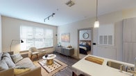 This 2-bedroom, 2-bathroom residence offers a thoughtfully designed single-level layout that balances comfort and functionality. The open-concept living area features hardwood-style flooring, a patterned area rug, track lighting, and large windows with blinds that invite abundant natural light. The space flows seamlessly into a modern kitchen equipped with stainless steel appliances — including a refrigerator, range, and microwave — alongside sleek light-wood cabinetry, a tile backsplash, and a generous white-countertop island with bar seating and pendant lighting overhead. An in-unit stacked washer and dryer adds everyday convenience. Both bedrooms are carpeted and feature ceiling fans, natural light from windows, and walk-in or reach-in closets. The primary bedroom includes an en-suite bathroom with a long vanity, white countertops, tile flooring, and a shower-tub combination. The second bathroom mirrors this clean, neutral aesthetic. A versatile second living area or flex space provides additional room for relaxing or working. Throughout, the warm, neutral color palette and contemporary finishes create a cohesive, welcoming ambiance well-suited for everyday living.